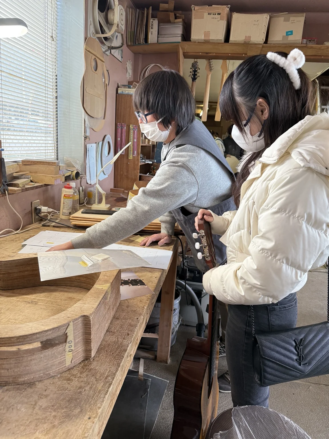 作業台の図面を指す人と、ギターを持って隣に立つ人。