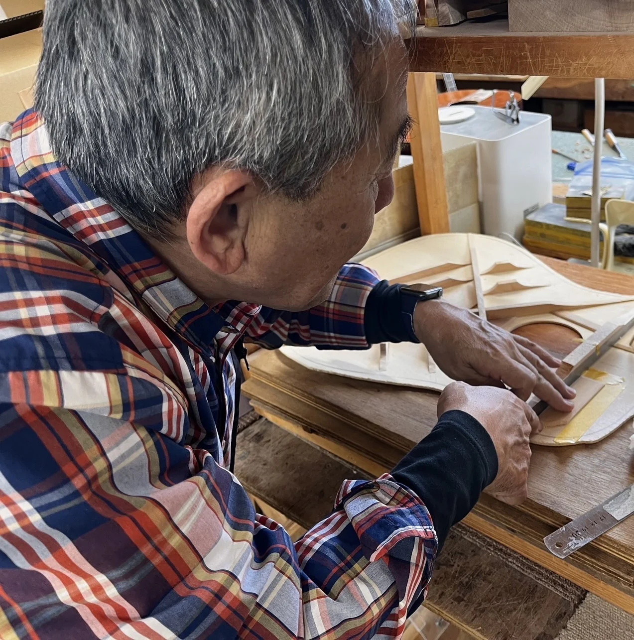 ギターの板の内側に木の部材を当て、手元を確かめる様子。