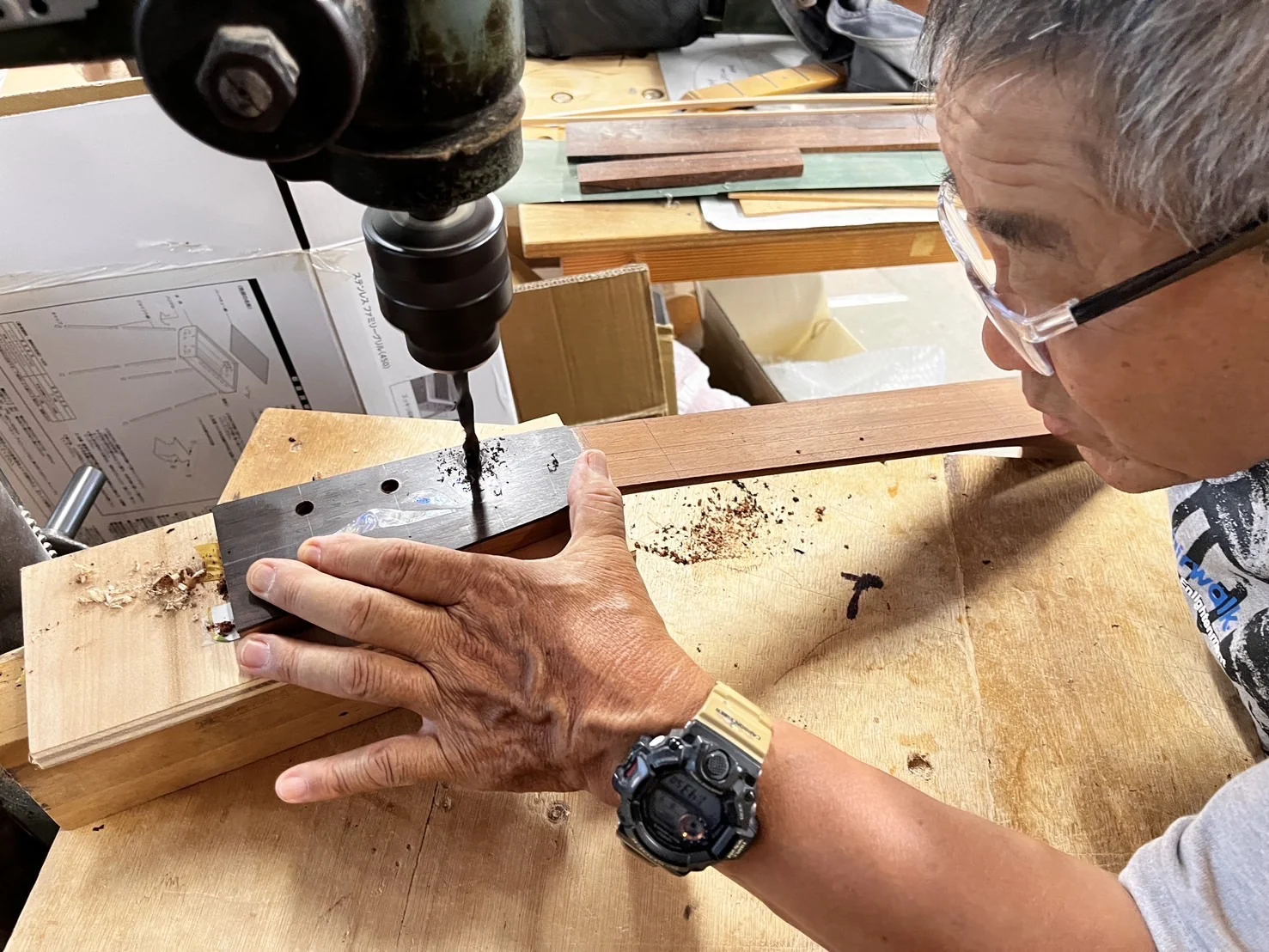 ボール盤の下でギターヘッドを支え、穴を開ける作業。