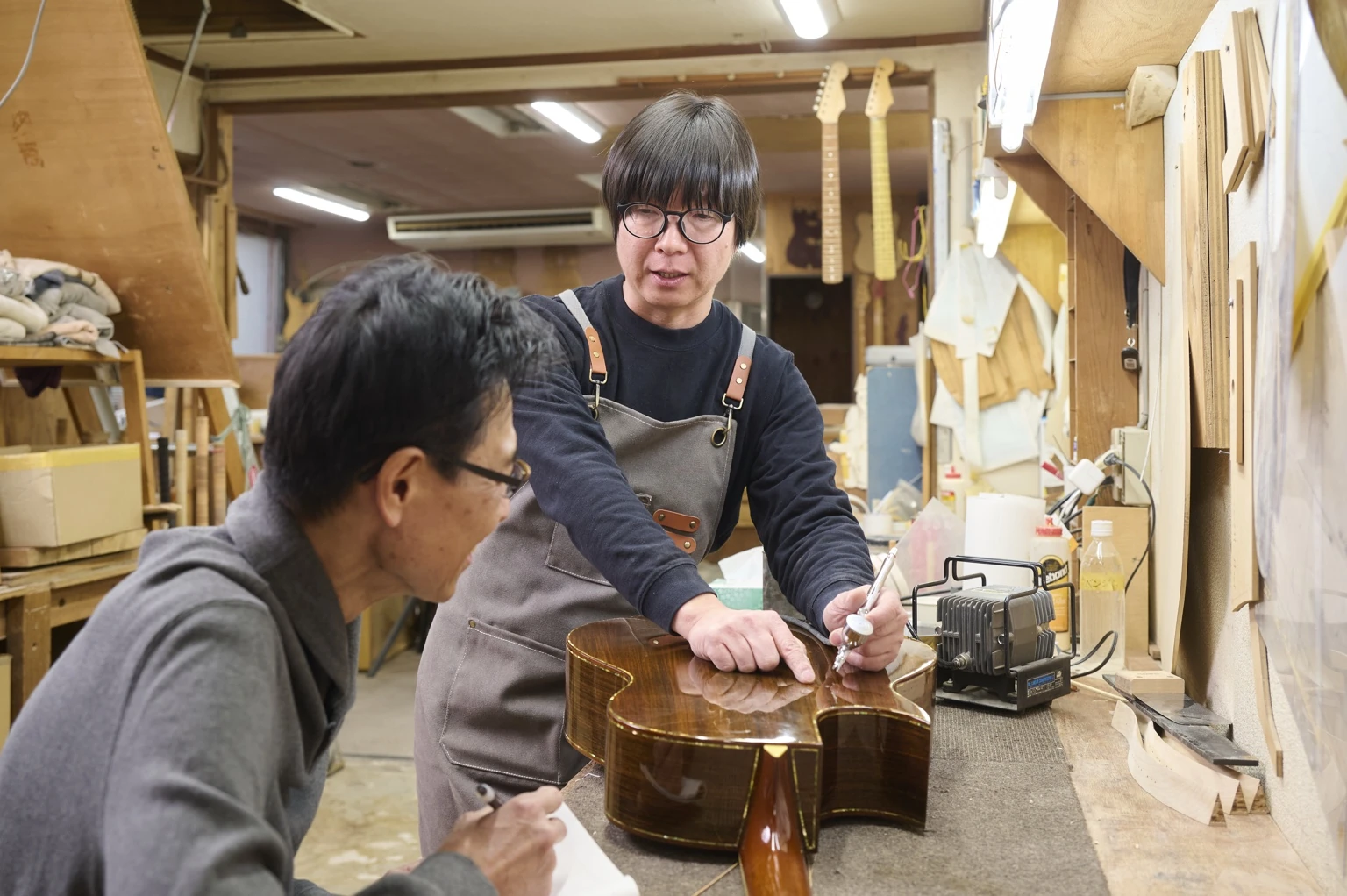 工房の作業台でギターを囲む2人。